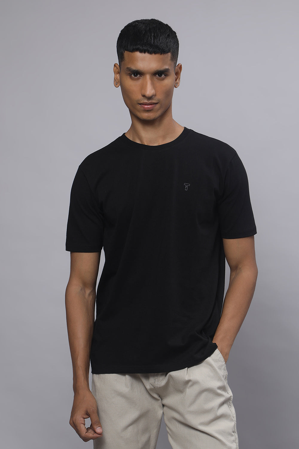 Man wearing a black t-shirt and beige pants against a gray background